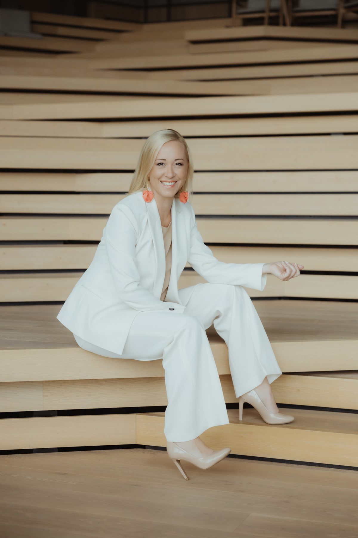 Sabine Kronberger sitzt im weißen Anzug auf einer hölzernen Stiege